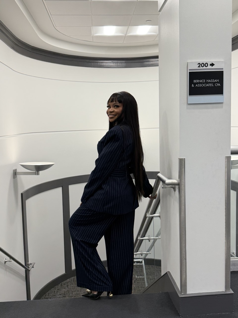 Bernice Hassan, CPA, standing on the landing outside the firm's Columbia, Maryland office, beside the directory sign reading 200, Bernice Hassan & Associates, CPA.