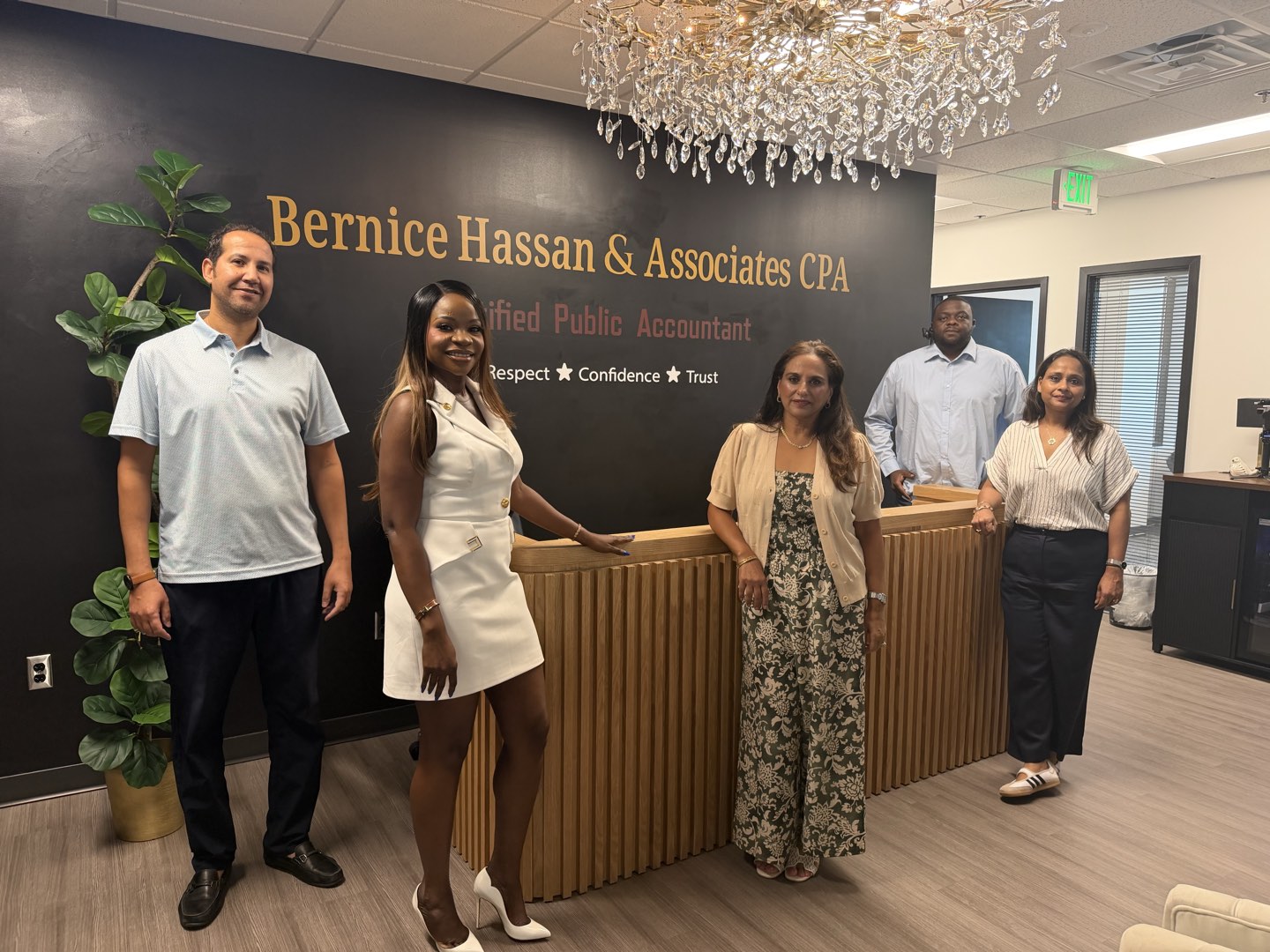 The five members of the Bernice Hassan & Associates CPA team standing full length at the reception desk of the firm's Columbia, Maryland office, beneath the wall lettering reading Respect, Confidence, Trust.